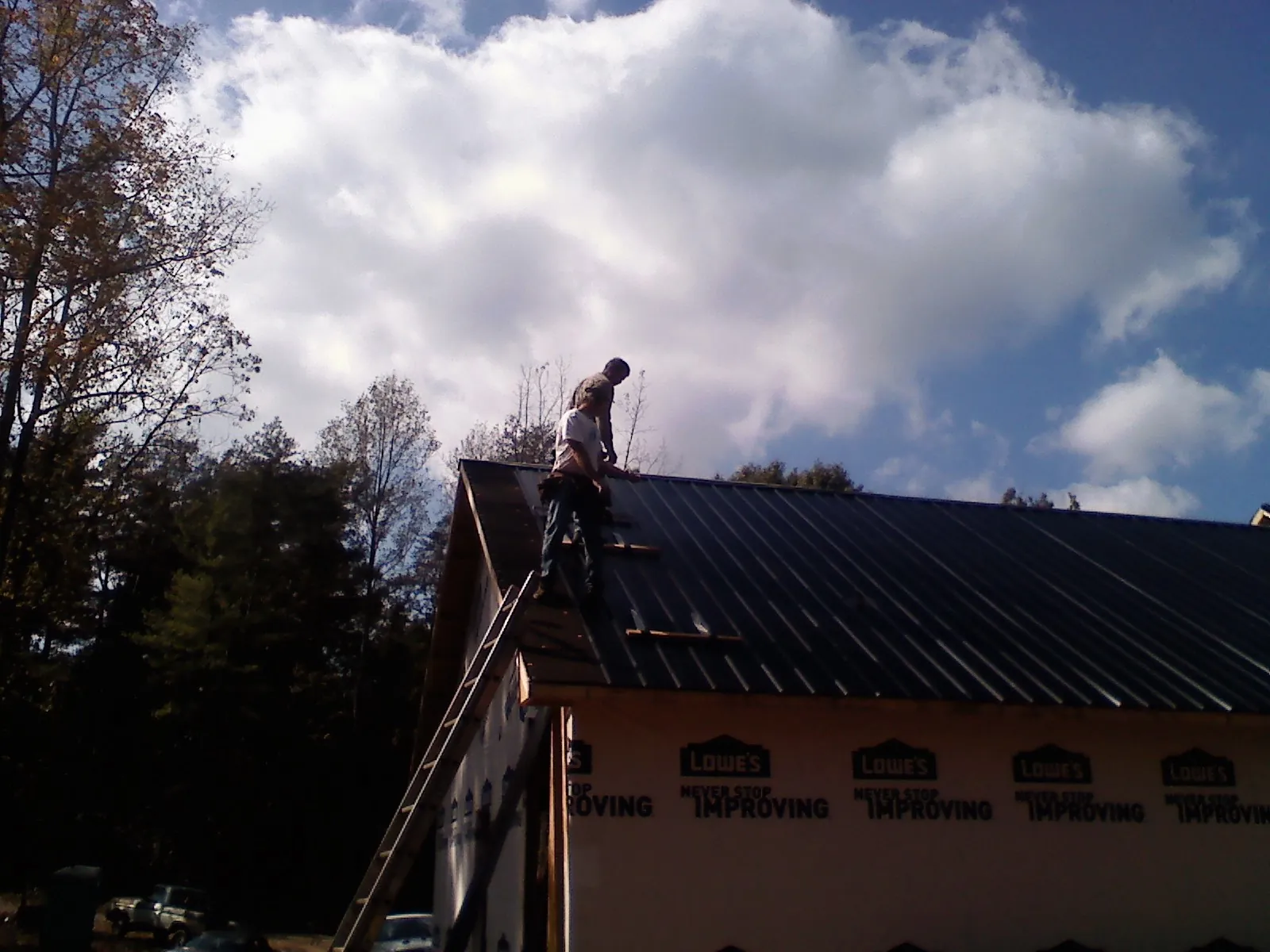 Roofer fastening dark metal panels high against a cloudy sky, from a Roof Inspection job in Roselle Park