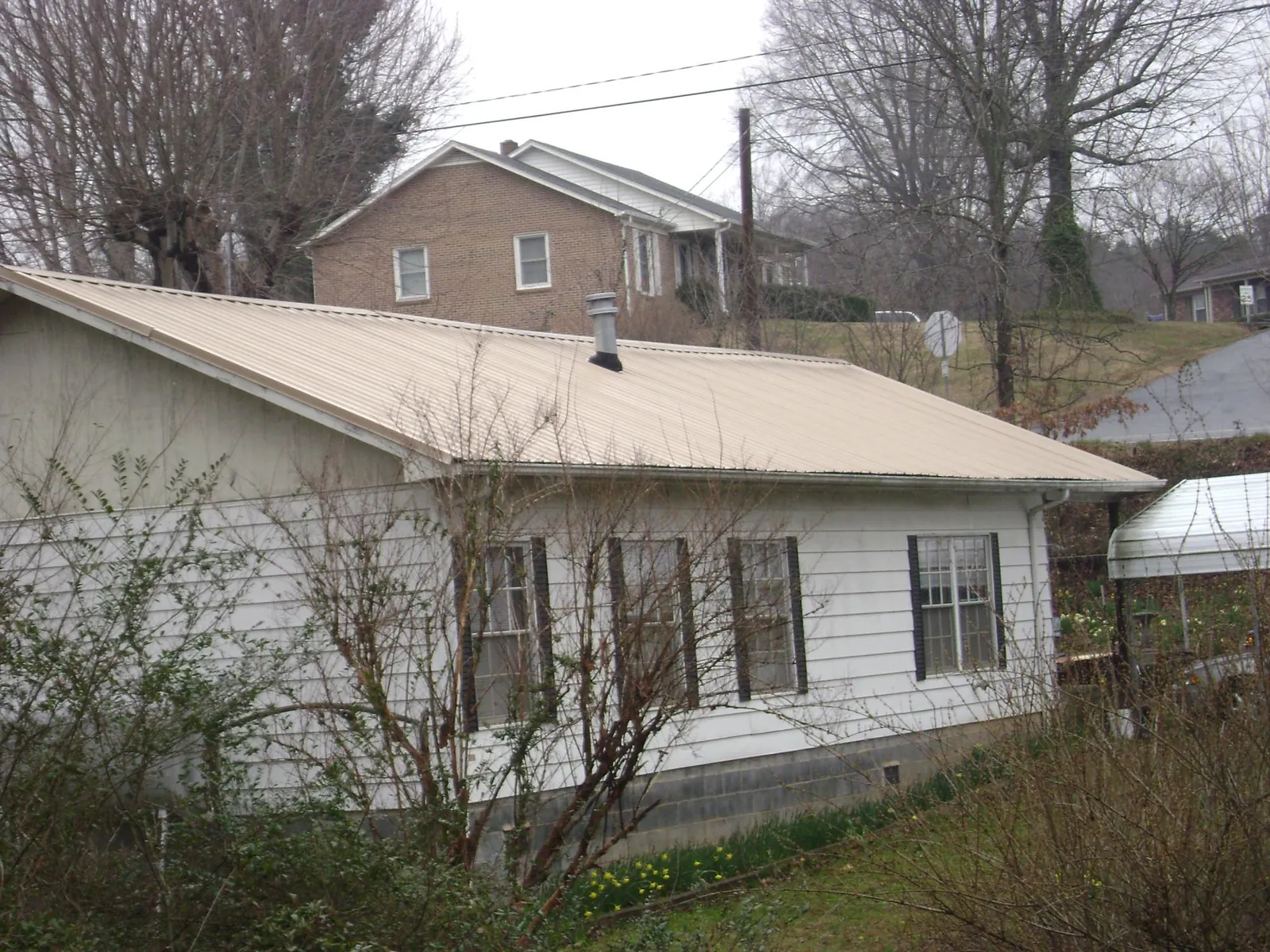 Tan metal roof on a white sided house set into a hillside — Commercial Roofing by Roofing Brothers in Roselle Park